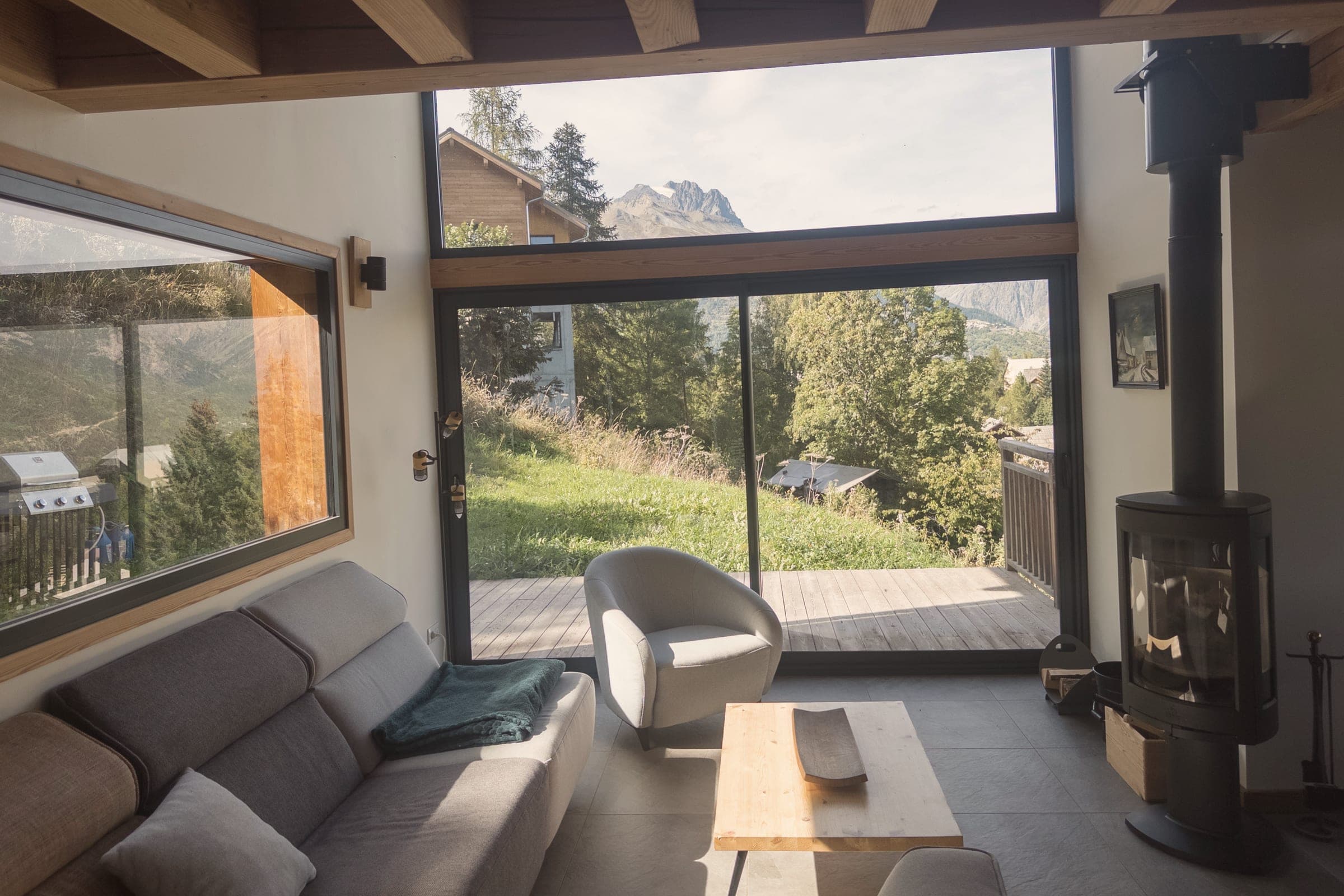 Le salon : canapé, poêle à bois et baie vitrée sur la terrasse